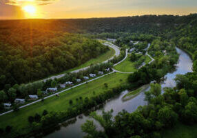 Aerial view of Eagle Cliff Campground along the Root River near Lanesboro, Minnesota, with campsites, green fields, winding roads, and forested bluffs at sunset.