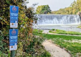 Talking Trail signs posted near the Lanesboro Dam, with the waterfall flowing in the background along the Root River.