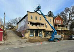A blue boom lift reaches the roofline of a historic multi-story building in downtown Lanesboro during an exterior renovation project.