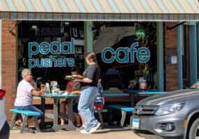 Server delivers plates of food to guests seated at outdoor picnic tables in front of Pedal Pushers Café in downtown Lanesboro, Minnesota.